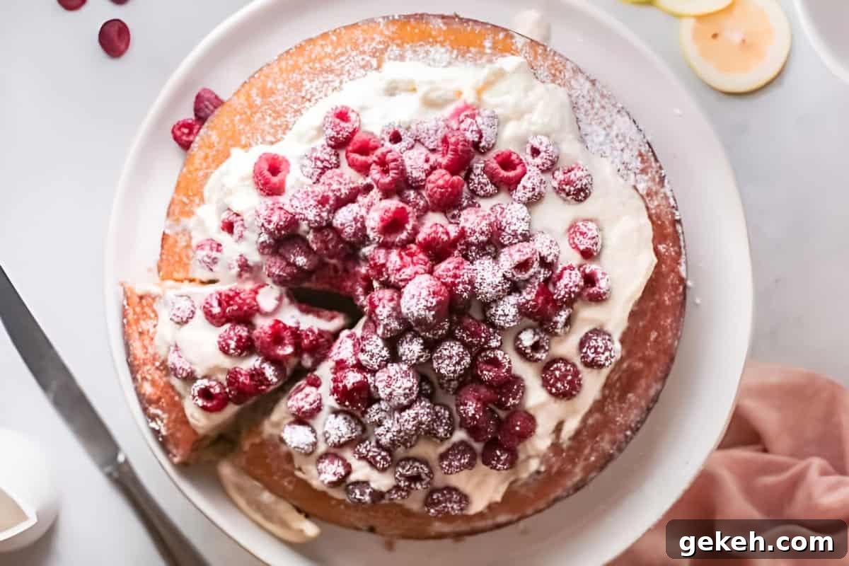 overhead view of raspberry olive oil cake topped with whipped cream and fresh raspberries on a cake stand.