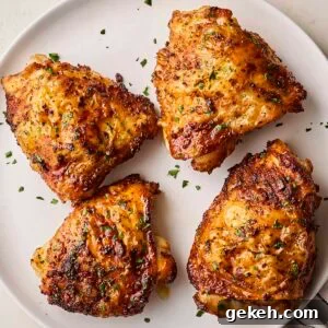 A white plate with four cooked, coated chicken thighs, ready to eat.