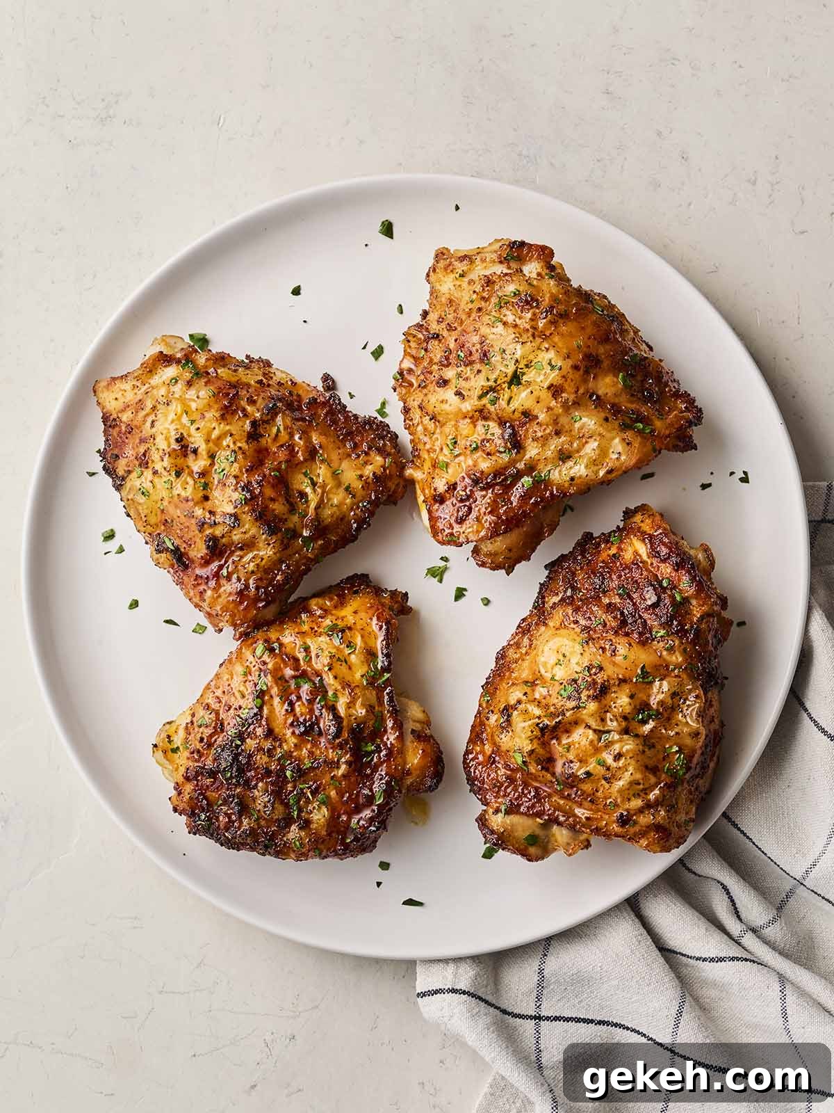 A white plate on a white surface with a tea towel and 4 chicken thighs ready to eat.