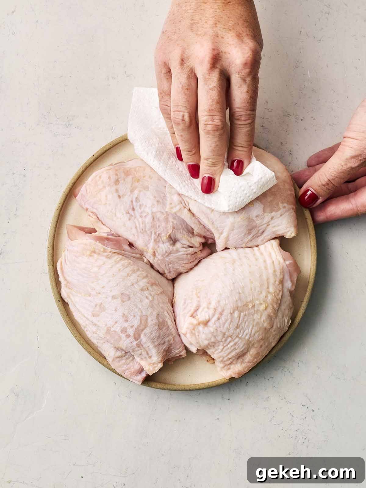Two hands dabbing chicken thigh skin with a paper towel.