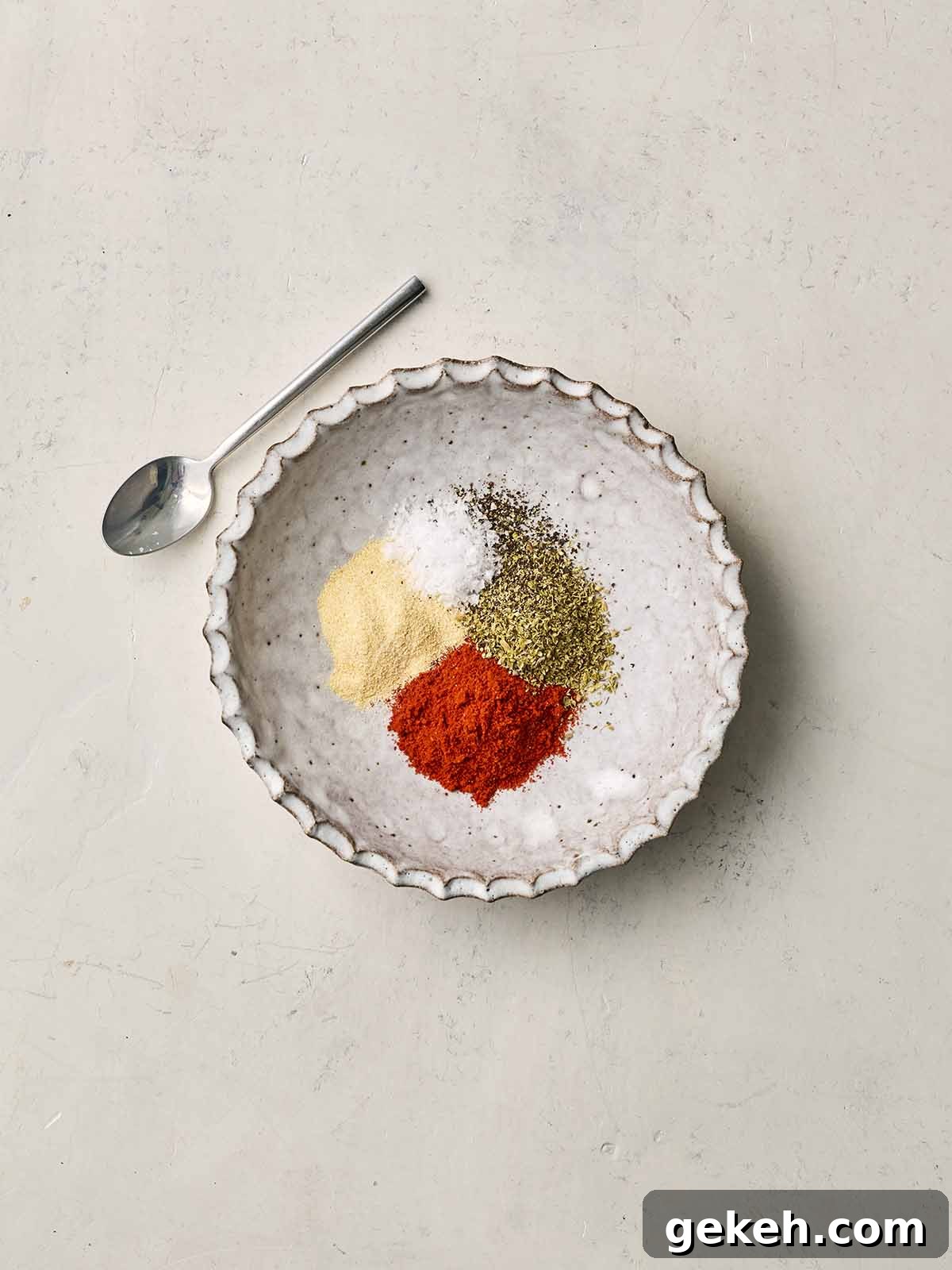 A white bowl with a spice mix inside and a spoon to the side.