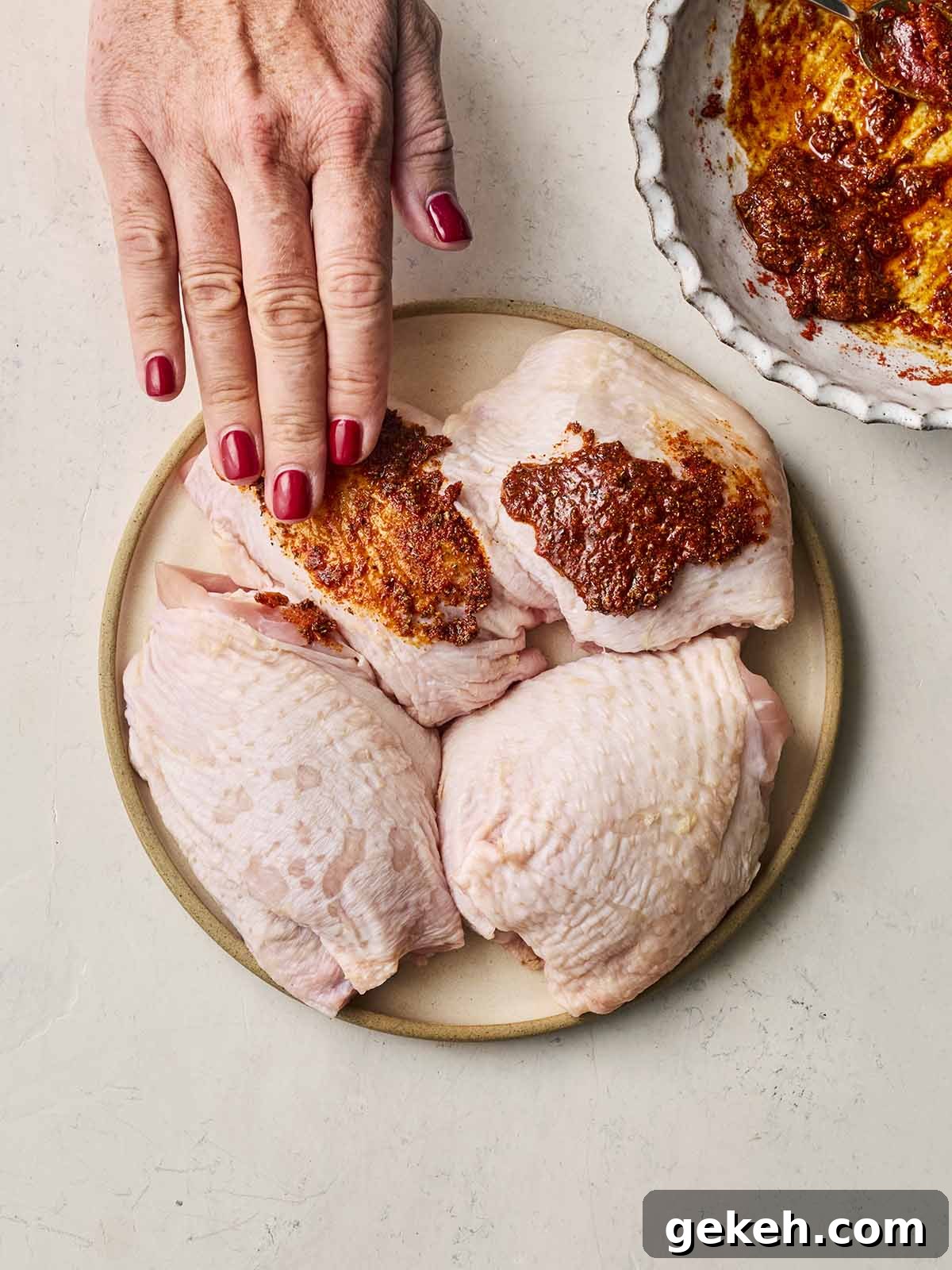 A plate of chicken thighs, with a hand rubbing an oily spice mix over the skins.