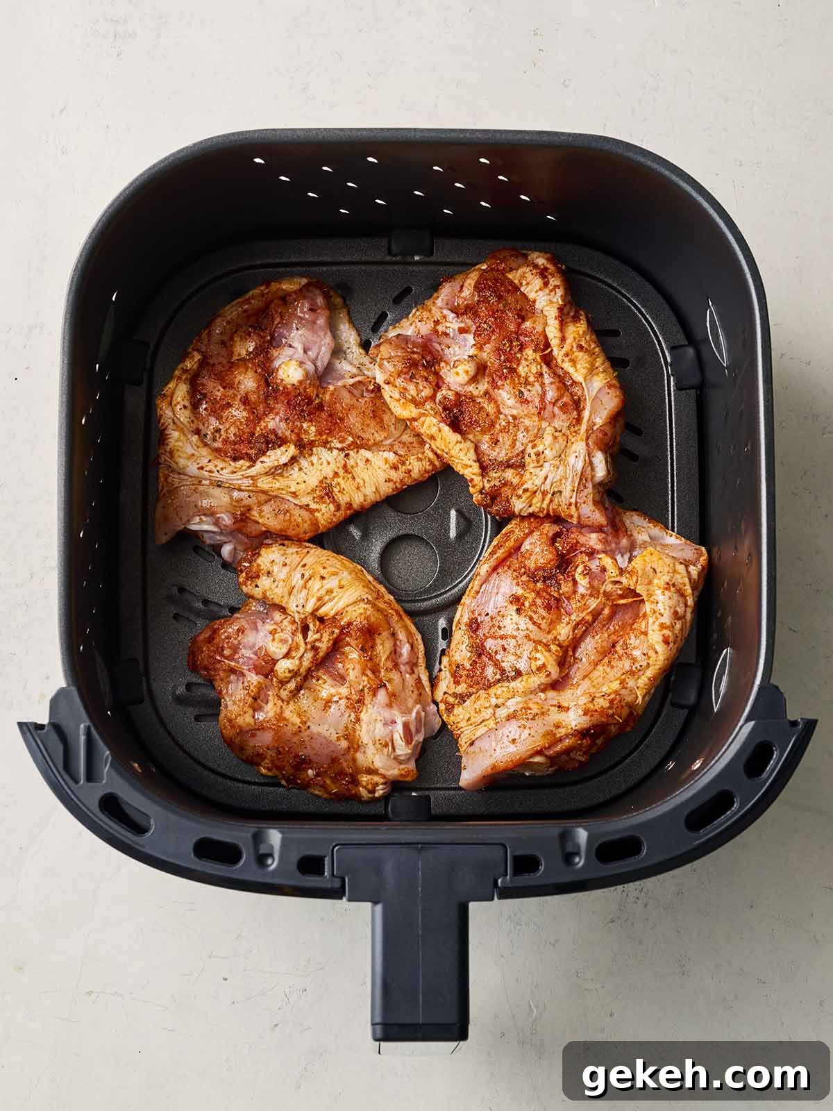 An air fryer grill with four marinaded chicken thighs, uncooked, inside.