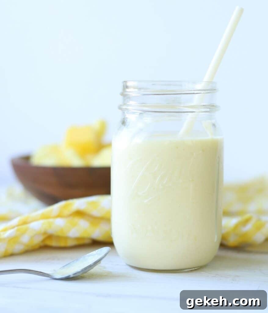 Refreshing Mango Pineapple Smoothie Recipe for Tropical Flavor 2 mango pineapple smoothie in a mason jar with a straw with yellow and white checkered napkin and wooden bowl full of mango and pineapple