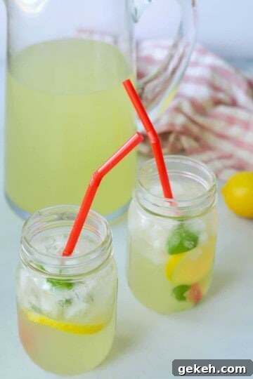 Two mason jars full of lemonade with a pitcher next to them.
