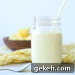 mango pineapple smoothie in a mason jar with a straw with yellow and white checkered napkin and wooden bowl full of mango and pineapple