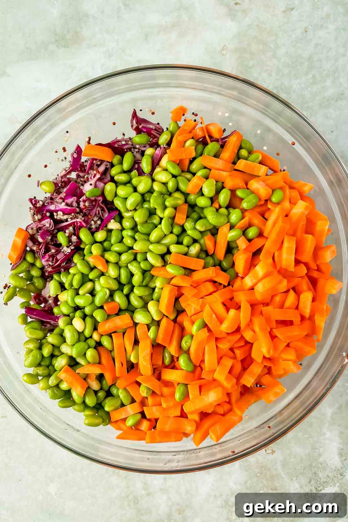 diced carrots, cooked edamame, shaved cabbage in glass mixing bowl. 