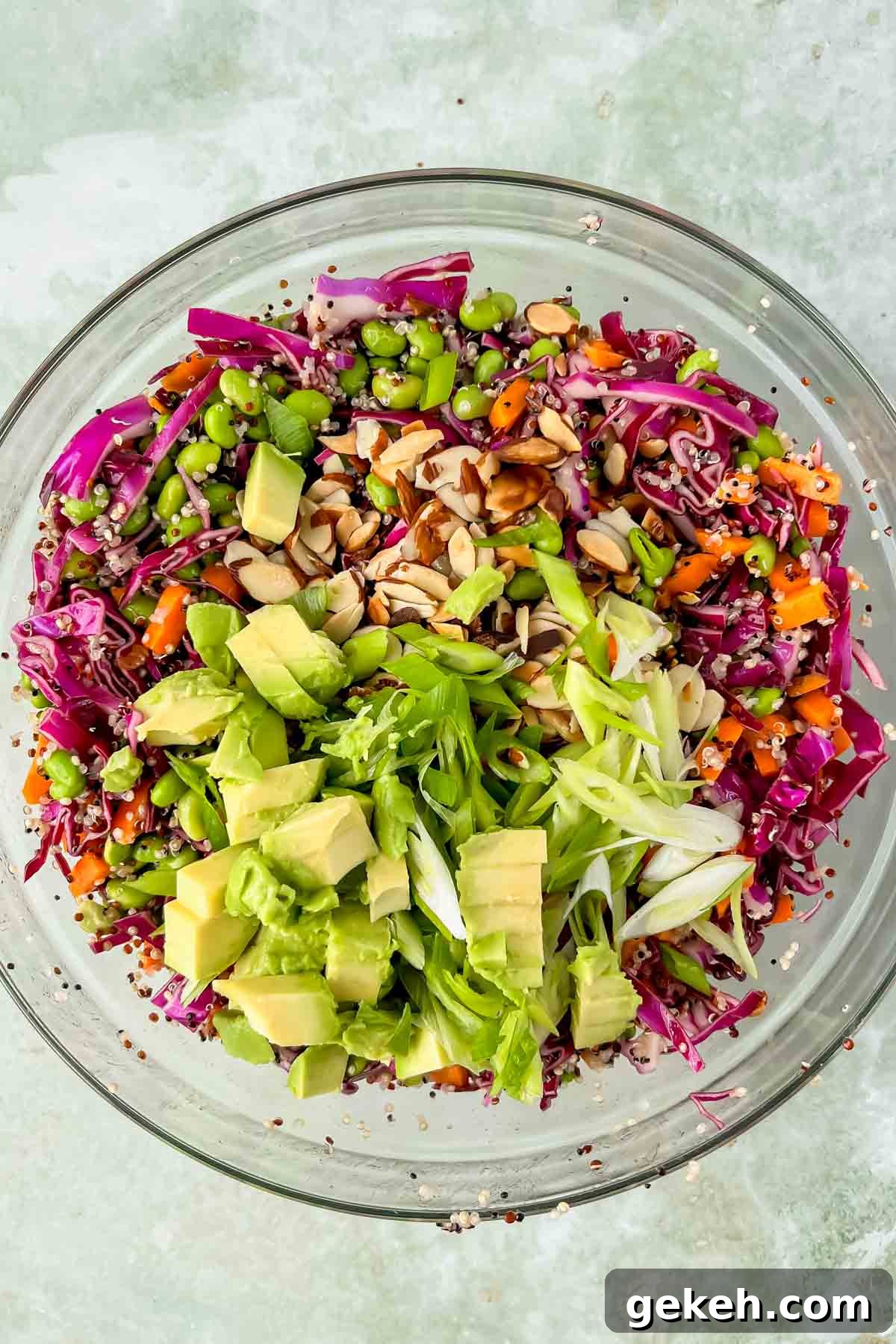 quinoa edamame salad topped with fresh avocado and green onions in large glass mixing bowl. 
