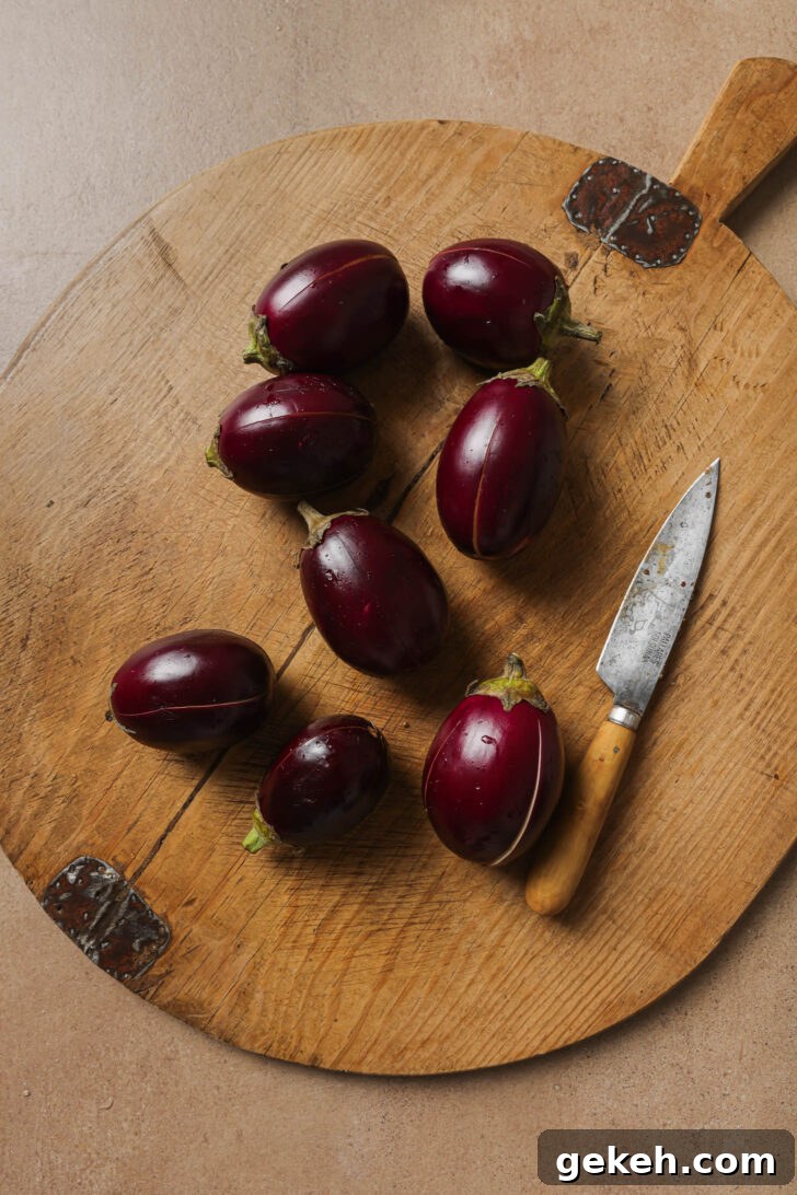 Bagara Baingan: Authentic South Indian Eggplant Curry Recipe 10 Slit baby eggplants on a wooden cutting board with a knife.