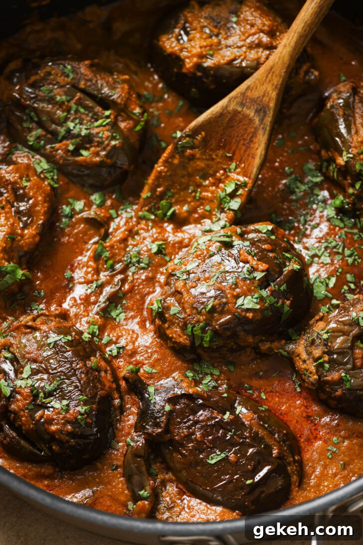 Bagara Baingan: Authentic South Indian Eggplant Curry Recipe 17 Close up of Bagare Baingan in a skillet with a wooden spoon garnished with minced cilantro.