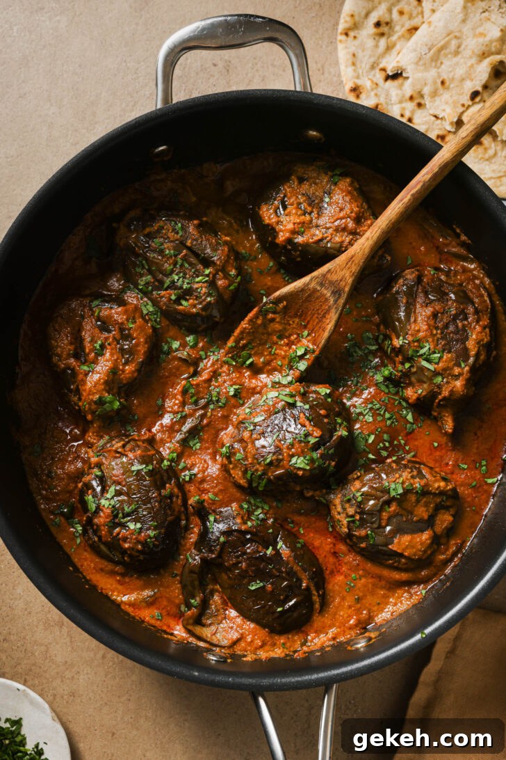Bagara Baingan: Authentic South Indian Eggplant Curry Recipe 3 Bagare Baingan in a skillet with a wooden spoon garnished with minced cilantro.