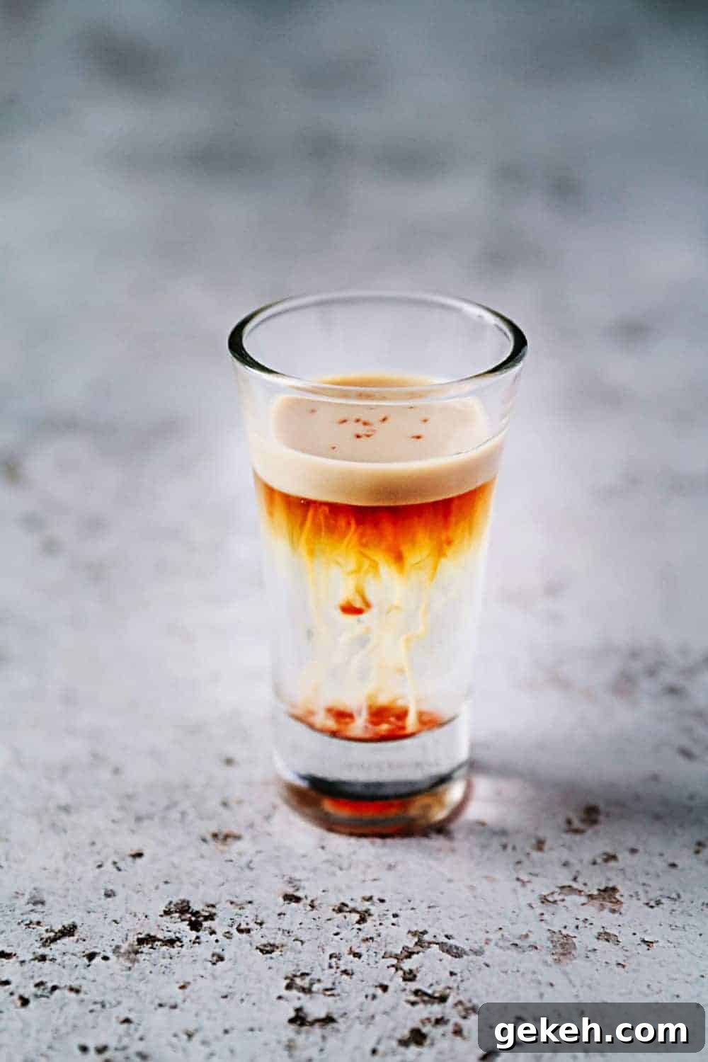 A small shot glass with jellyfish beverage sitting on a gray counter