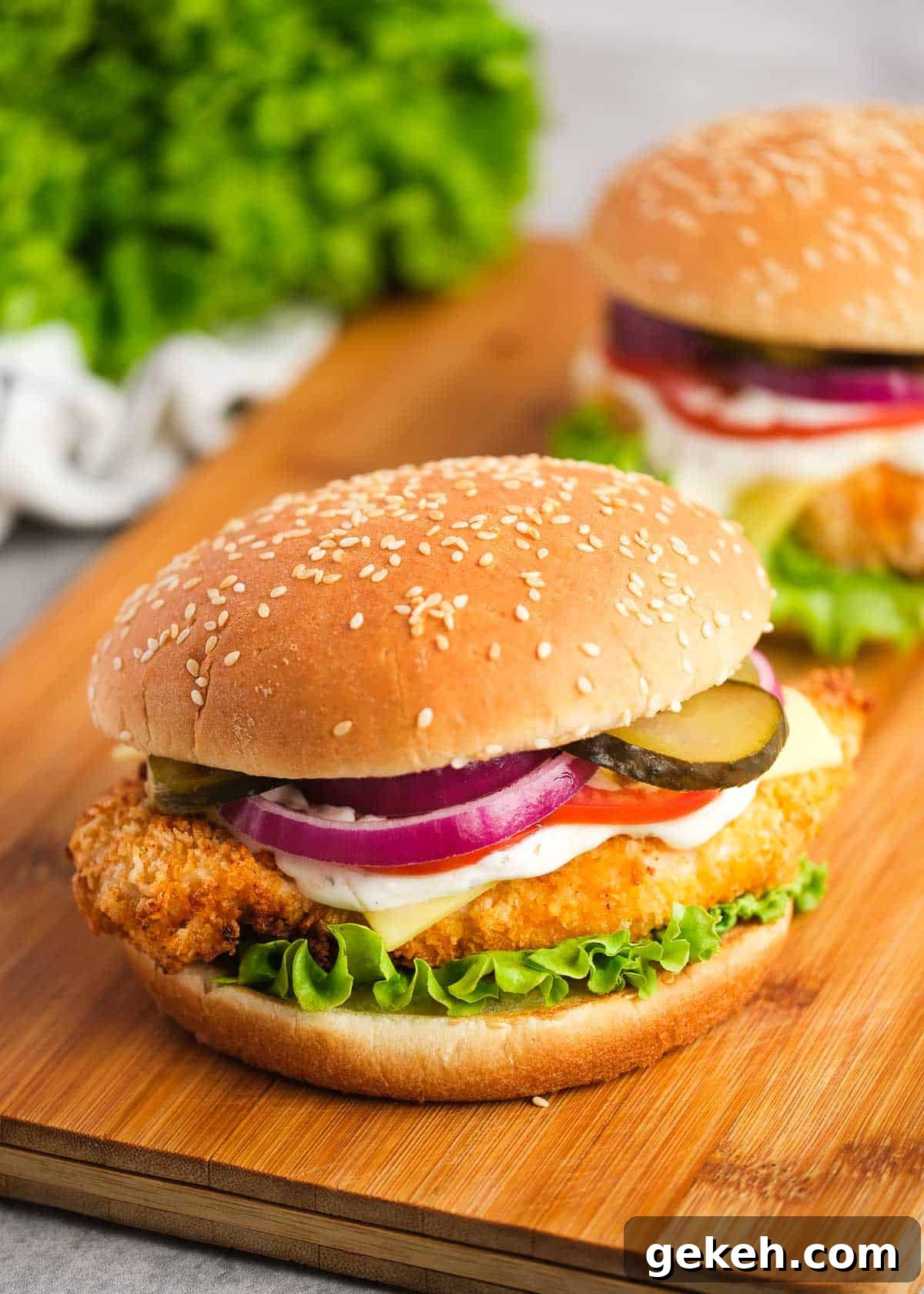 Crispy Air Fryer Chicken Sandwich Recipe 13 two loaded chicken sandwiches on a wooden cutting board with pickles, tomatoes, red onions, mayonnaise, cheese, and lettuce with a sesame bun