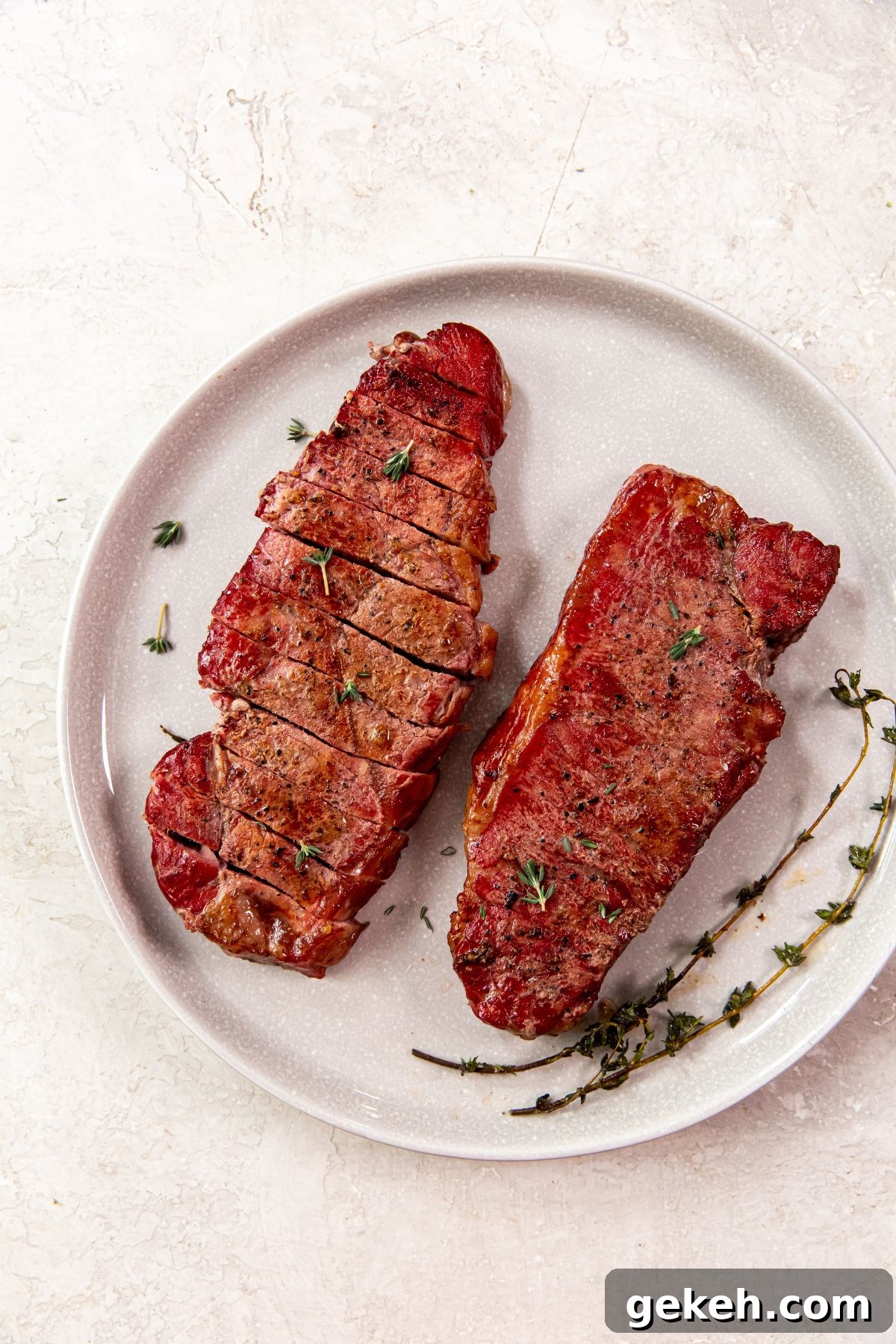 Smoked New York Strip Steak Recipe for Tender, Flavorful Results 2 Smoked New York Strip Steaks on a white plate with herbs