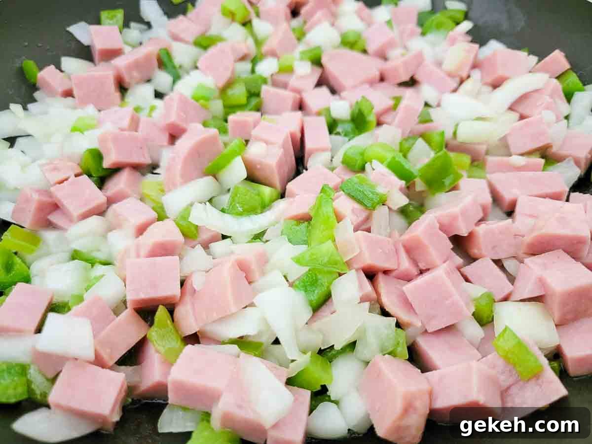Savory Spam and Scrambled Eggs Recipe for Quick Breakfast 4 diced spam, diced onions, and diced green peppers cooking in a skillet.