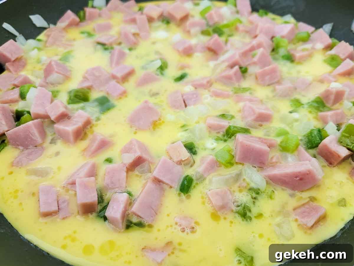 Savory Spam and Scrambled Eggs Recipe for Quick Breakfast 5 eggs, milk, diced spam, diced onions, and diced green peppers cooking in a skillet.