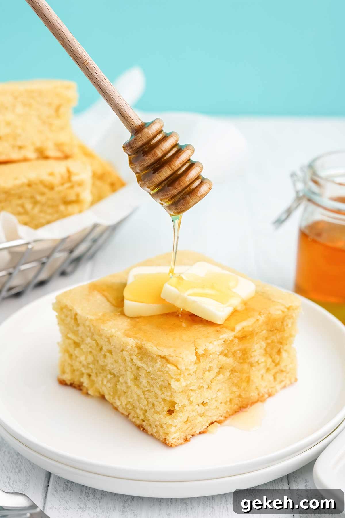 Square of cornbread with honey on a white plate with honey drizzling on top.