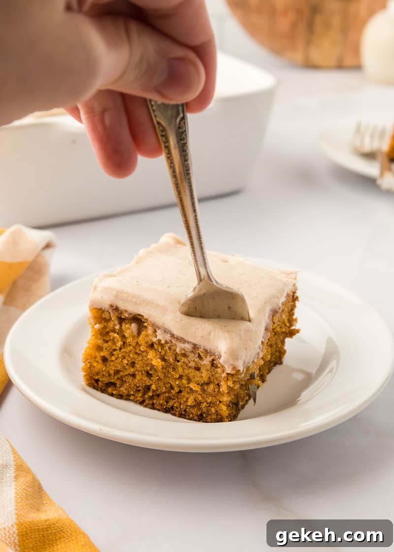 Moist Pumpkin Sheet Cake Recipe with Cream Cheese Frosting 20 A person using a fork to eat a piece of pumpkin cake.