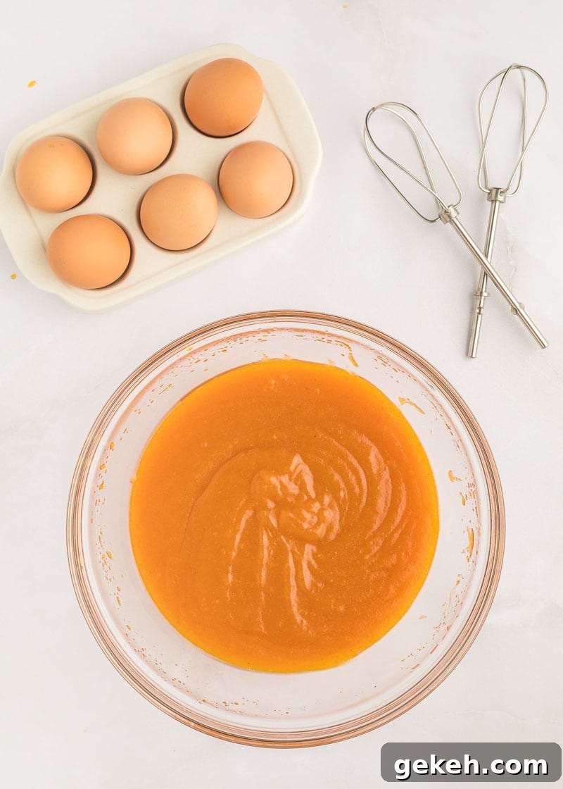 Moist Pumpkin Sheet Cake Recipe with Cream Cheese Frosting 7 A glass mixing bowl with canned pumpkin next to eggs and hand-beater whisks.