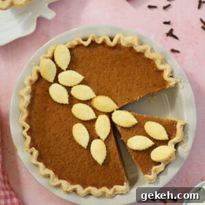 A gluten free pumpkin pie on a pink backdrop with cinnamon sticks and cloves surrounding it.