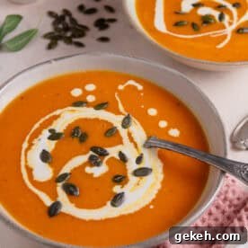 A bowl of roasted pumpkin soup with swirls of cream and pumpkin seeds on top.