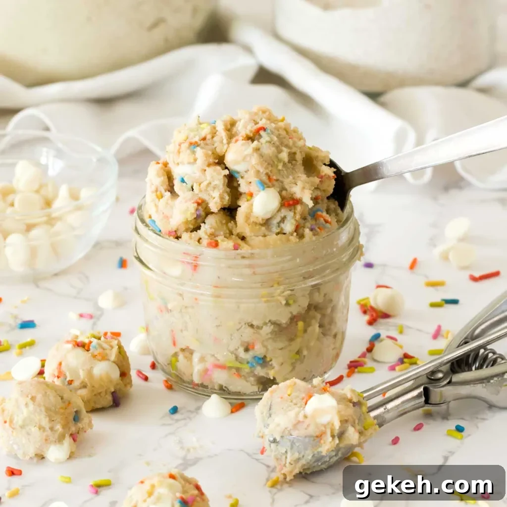 A small mason jar full of edible funfetti cottage cheese cookie dough with white chocolate chips with a cookie scoop.
