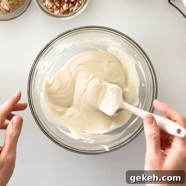Mixing yogurt ingredients to a glass mixing bowl with a spatula.