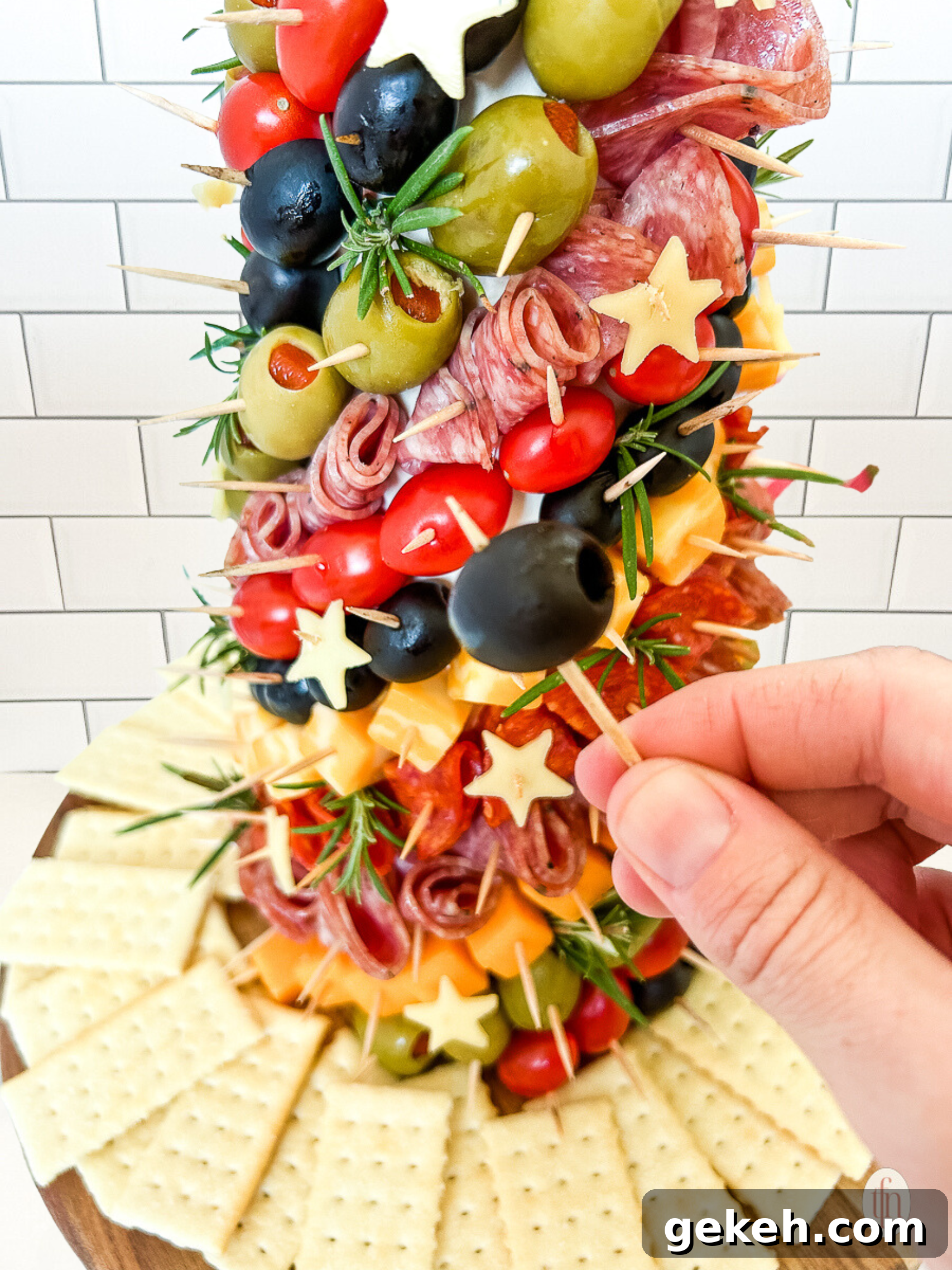 Festive Charcuterie Tree Guide: How to Build a Showstopping Holiday Platter 9 Holding an olive on a toothpick in front of a tree.