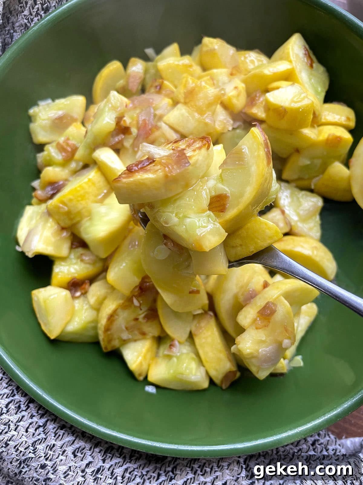 Perfectly Sautéed Summer Squash with Garlic and Herbs 2 A green bowl filled with sauteed yellow squash and onions and some being scooped on a spoon.