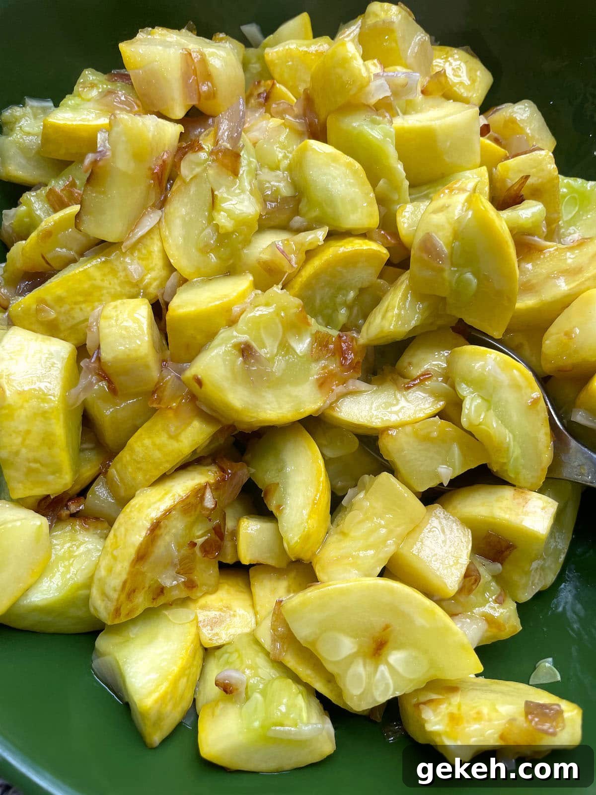 Perfectly Sautéed Summer Squash with Garlic and Herbs 6 A green bowl with a spoon filled with sauteed yellow squash and onions.