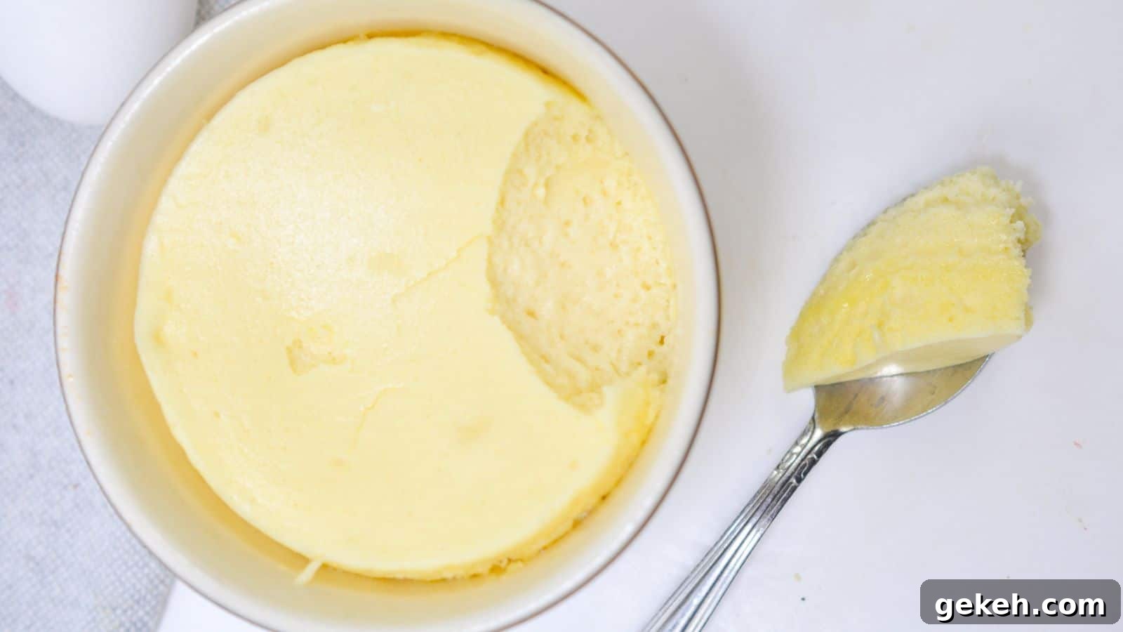 19 Desserts for Two to Share Straight from the Pan 14 A ramekin of creamy, smooth cheesecake with a spoon resting beside it, taking out a scoop on a white background.