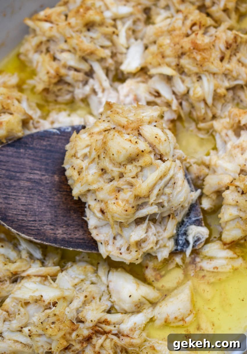 Jerry’s Place Baked Lump Crab Cakes Recipe (Copycat) 6 a wooden spatula lifting a baked lump crab cake out of a butter filled white baking dish