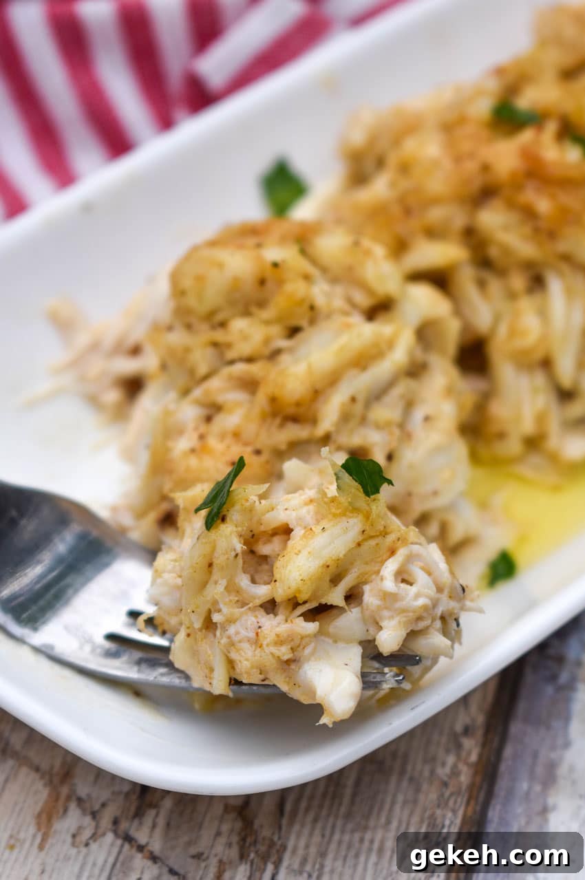 Jerry’s Place Baked Lump Crab Cakes Recipe (Copycat) 9 a silver fork holding a piece of a baked lump crab cake resting on the edge of a white serving plate