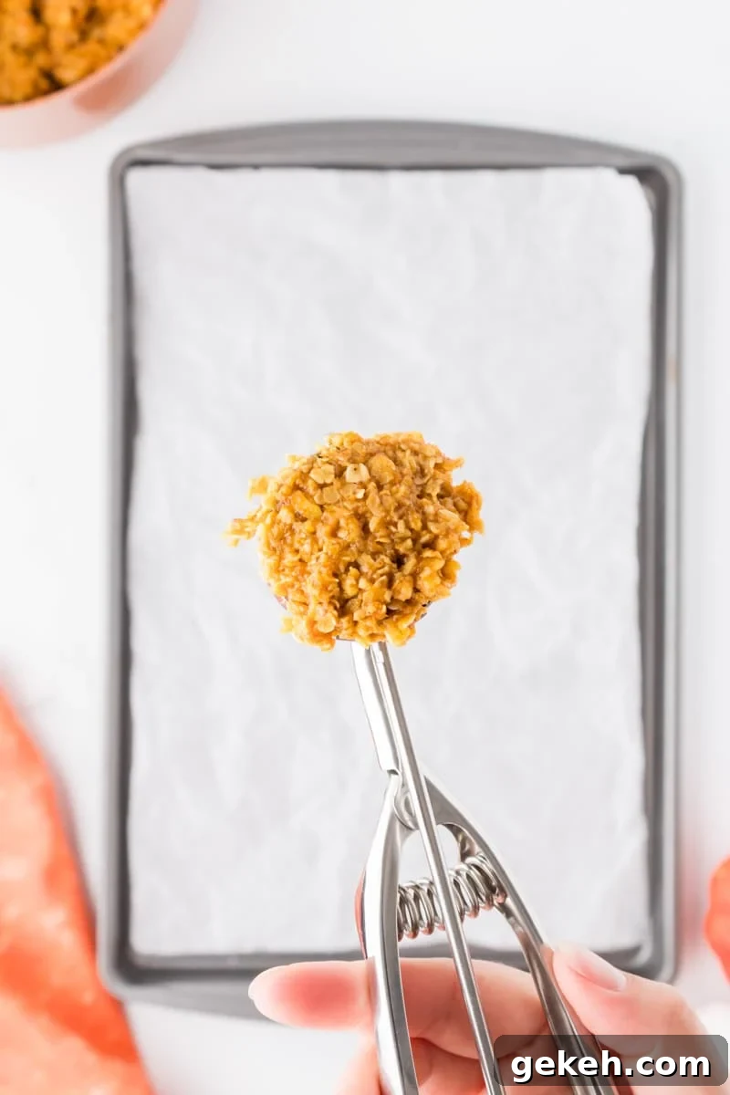 No-Bake Pumpkin Oat Cookies: Quick Fall Treats 8 A cookie scoop with an oatmeal mixture hovering over a parchment lined baking sheet.