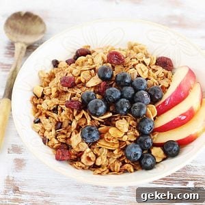 Whitish table with white bowl with granola and fruit, a wooden spoon beside it.
