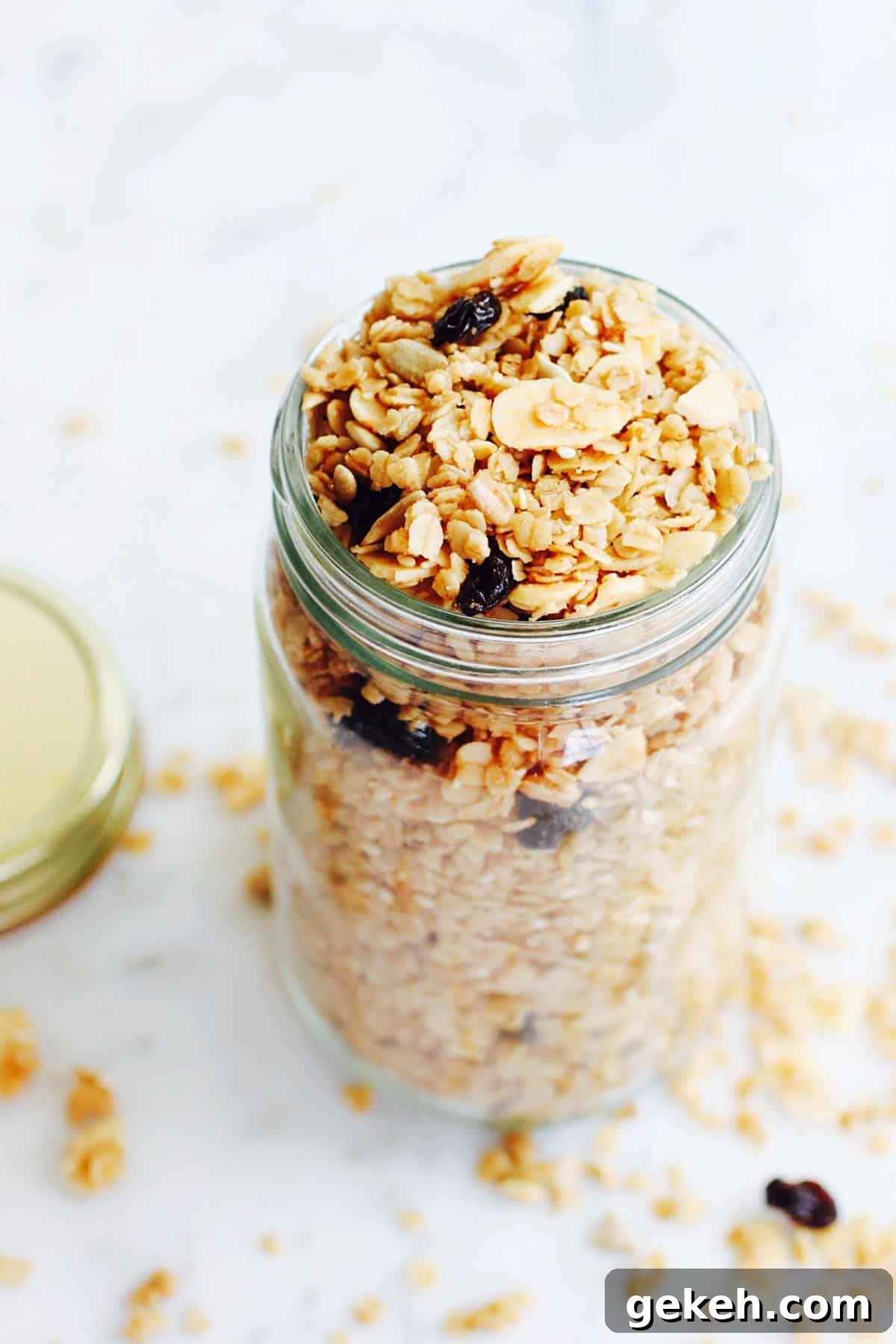 Tall glass jar with granola on a white surface.