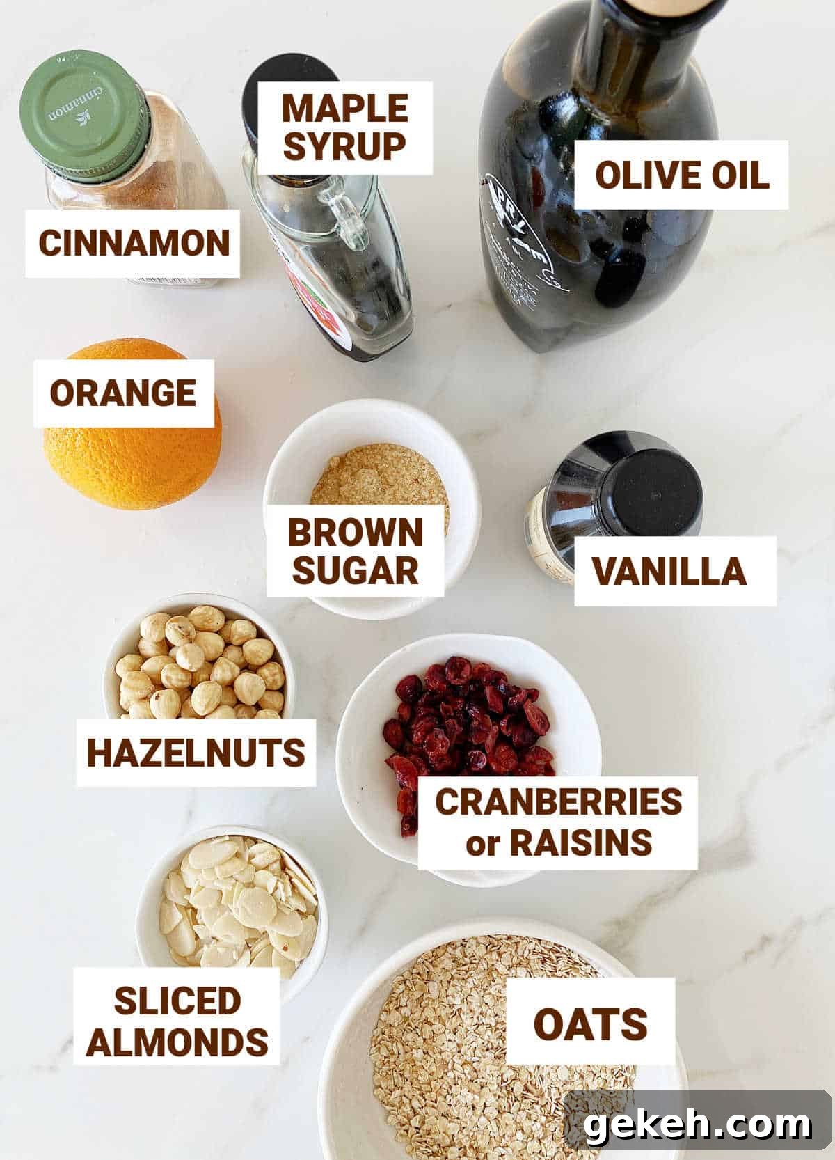 White surface with bowls containing ingredients for granola, including olive oil, maple syrup, orange, nuts and cranberries.