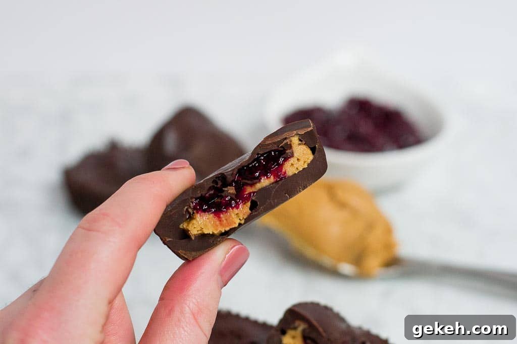 Hand holding half of a chocolate peanut butter cup filled with red berry chia jam.