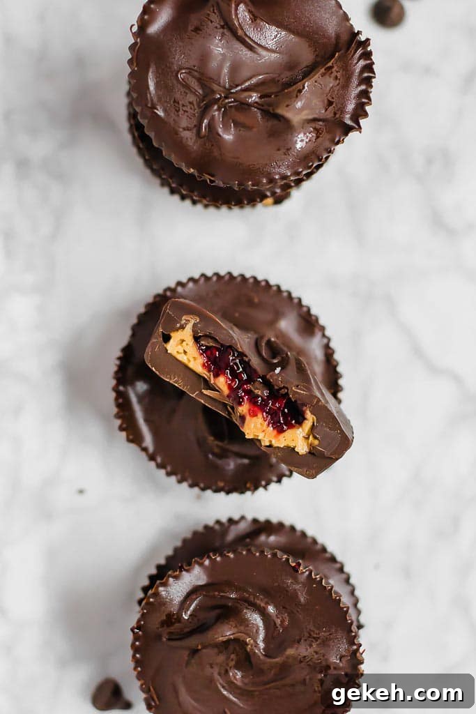 Three chocolate chia jam peanut butter cups in a vertical line on a marble table, middle cut in half to show layers.