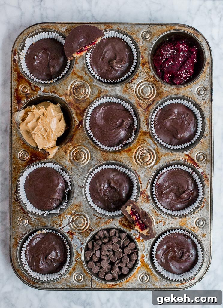 Muffin tin with chocolate peanut butter cups, some wells showing jam and peanut butter layers.