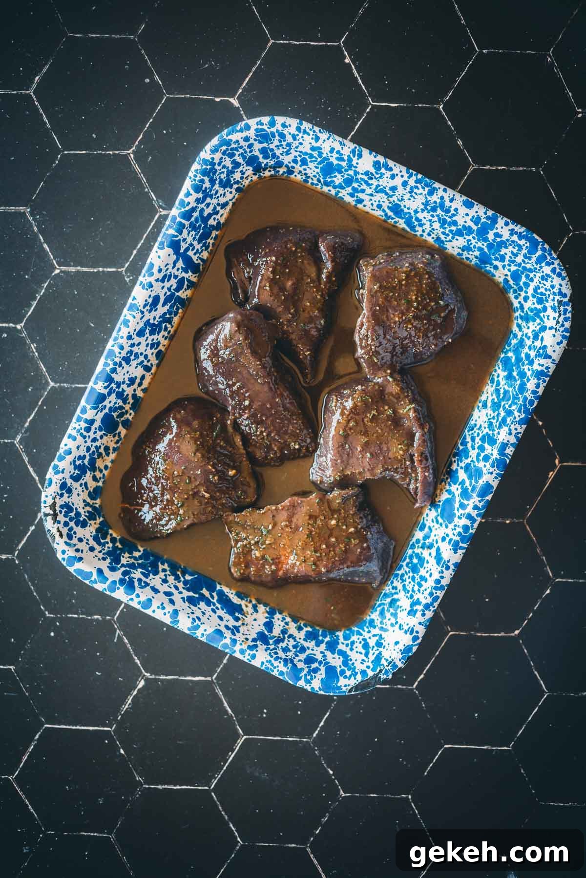 Grilled Elk Steaks: Juicy Elk Steak Recipe and Cooking Tips 5 A blue-speckled tray contains six pieces of marinated elk in a balsamic marinade.