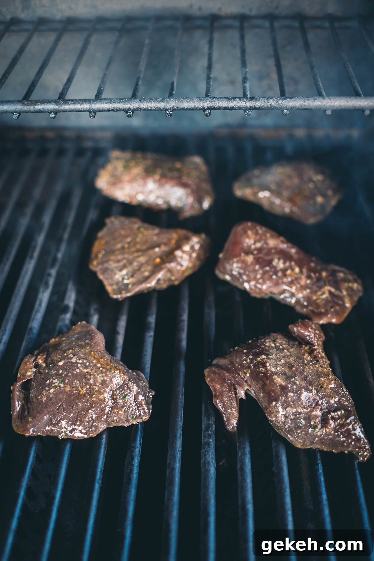 Grilled Elk Steaks: Juicy Elk Steak Recipe and Cooking Tips 6 Six pieces of marinated elk steaks being grilled on a barbecue with visible grill marks.