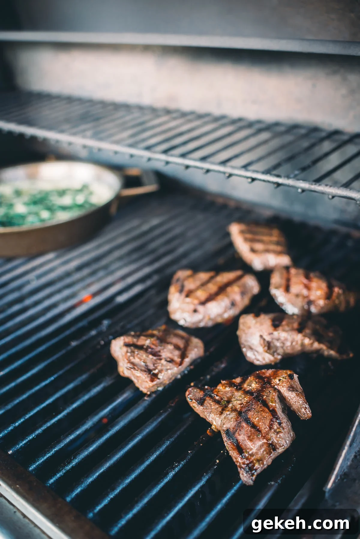 Grilled Elk Steaks: Juicy Elk Steak Recipe and Cooking Tips 7 Several elk steaks are grilling on a barbecue. A skillet with vegetables is also visible in the background.