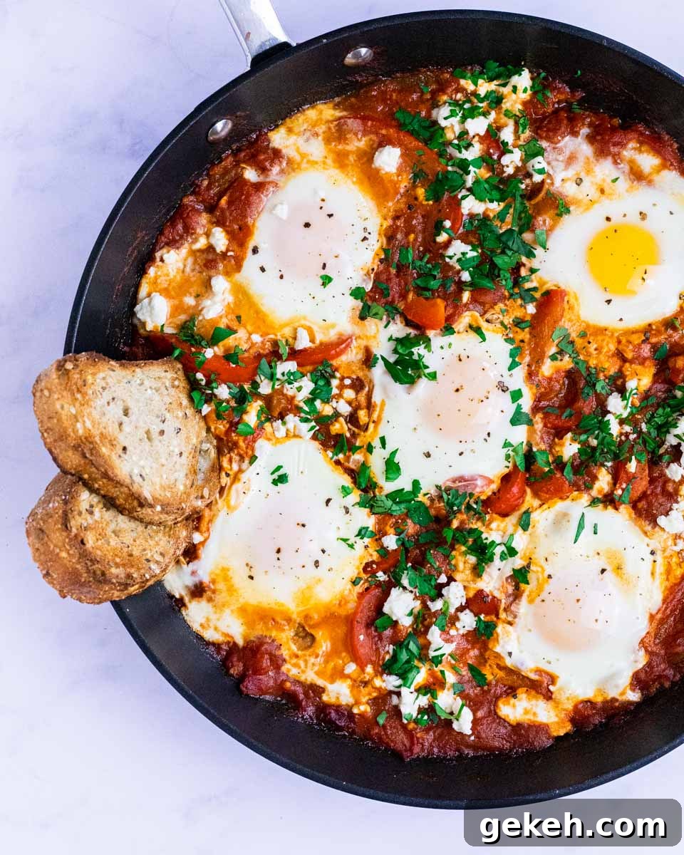 A top down view of a skillet of shakshouka with toasted bread dipped into it.