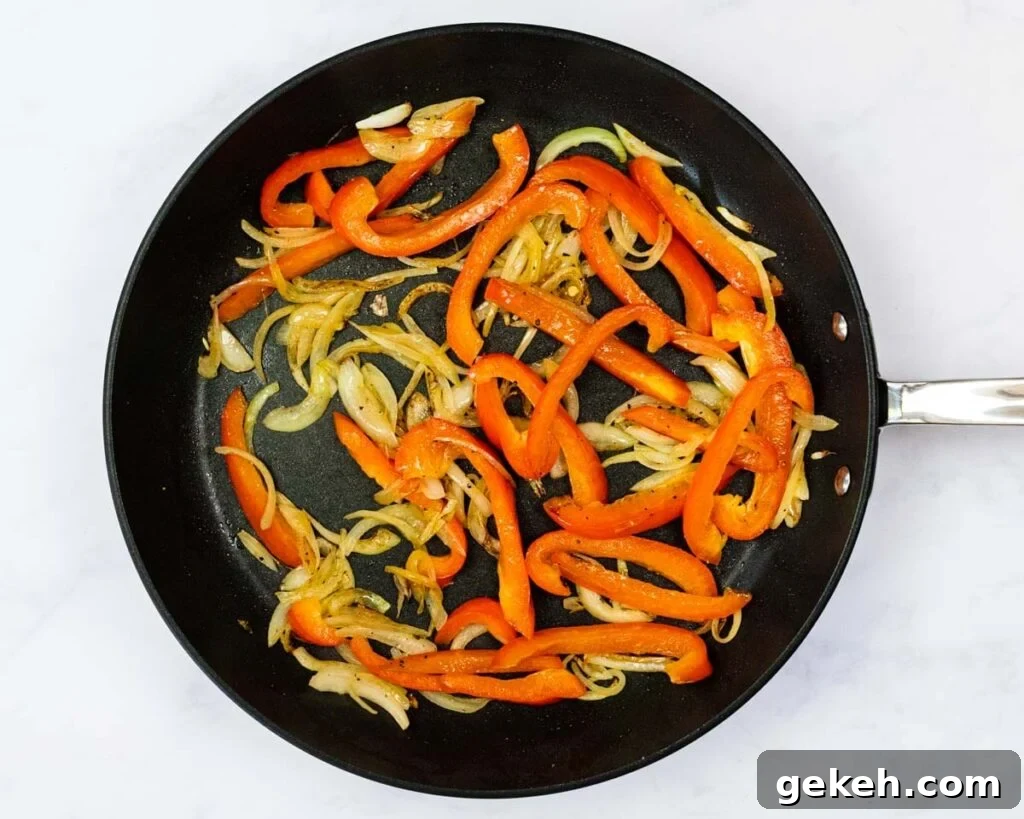 A top down view of sauteed peppers and onions in a skillet.
