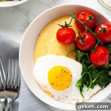 A close up view of a bowl of polenta topped with a fried egg, spinach and tomatoes.