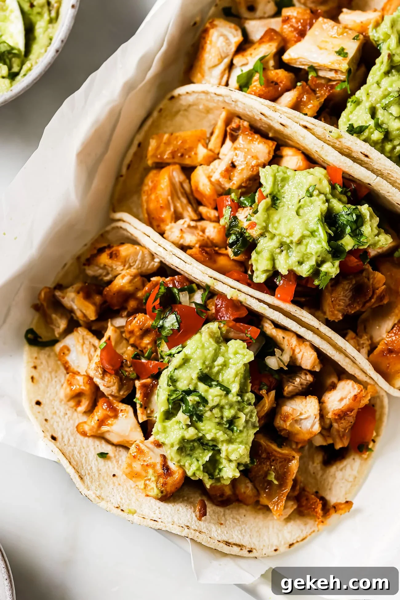 Chicken Tacos with Savory Homemade Marinade 10 Three chicken tacos topped with Pico de Gallo and guacamole on parchment paper.