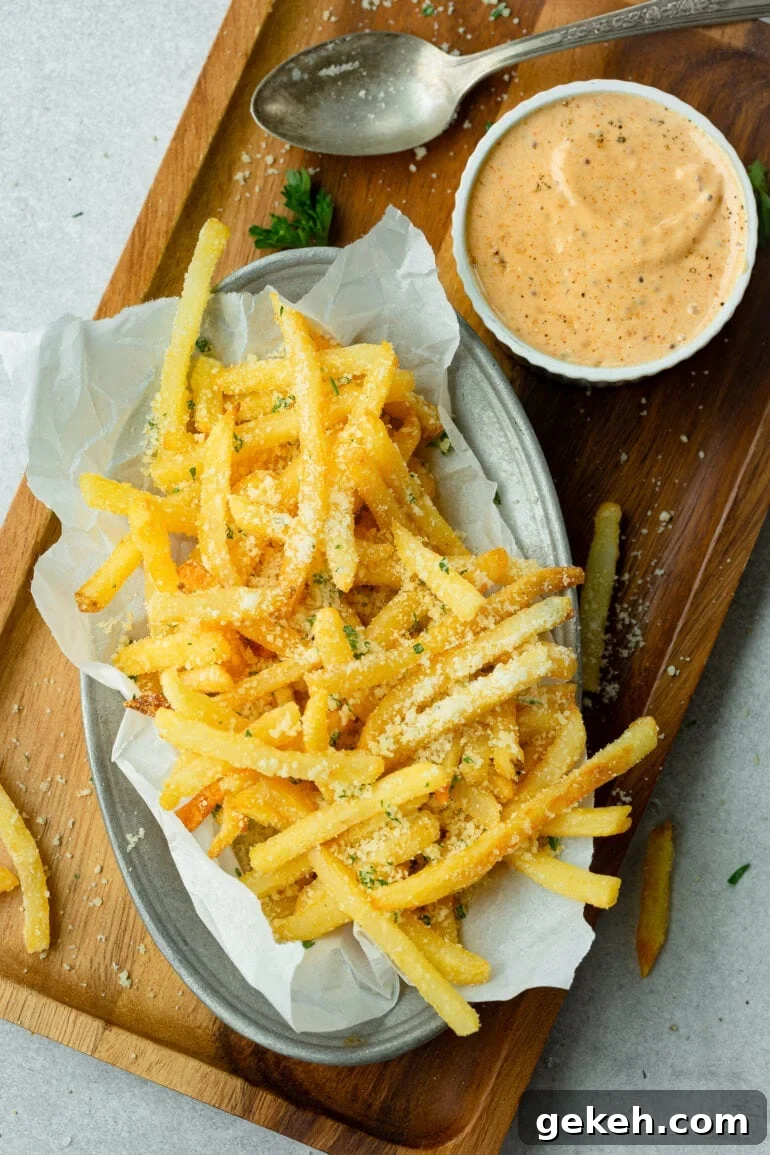 How to Make Disneyland-Style Pomme Frites at Home 2 a photo of a dish full of hot salty parmesan fries with a dish of cajun dipping sauce sitting next to it.