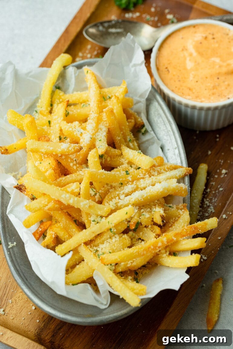 How to Make Disneyland-Style Pomme Frites at Home 6 a photo of a plate of hot salty pomme frites covers in parmesan cheese sitting next to a small bowl full of a cajun dipping sauce.