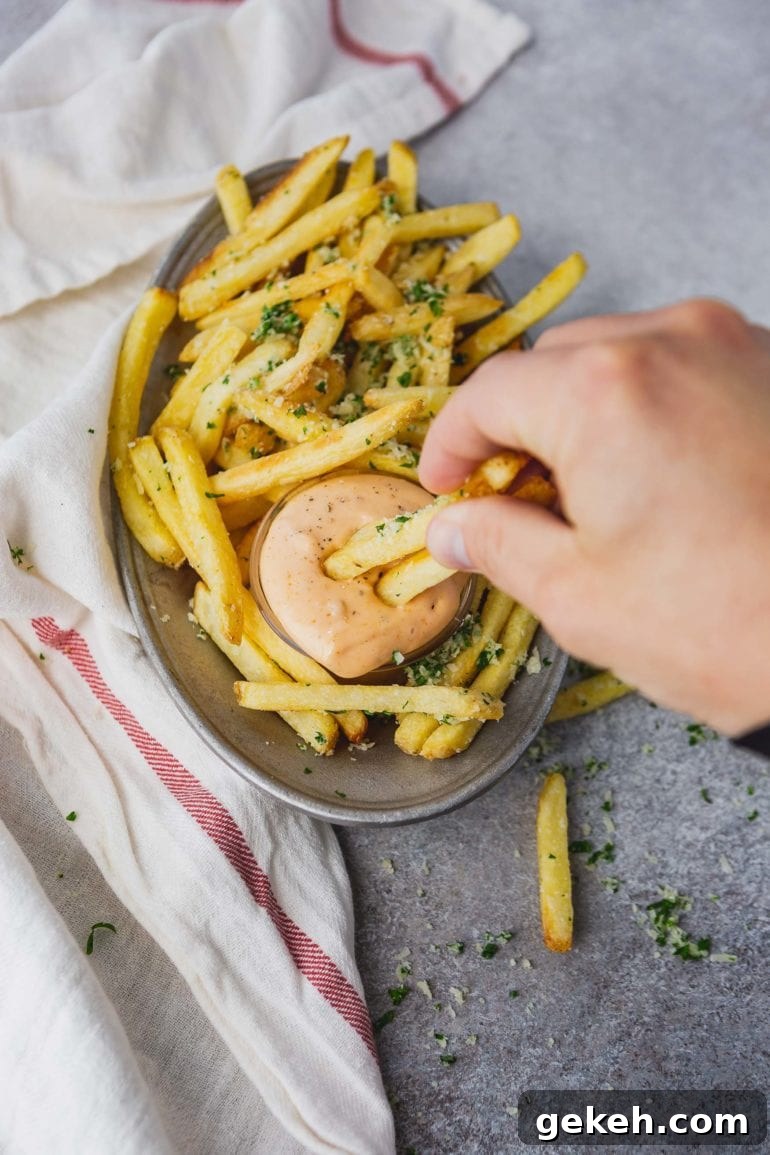 How to Make Disneyland-Style Pomme Frites at Home 7 a photo of a plate of golden pomme frites with a cup of cajun dipping sauce with someone dipping two fries in it.